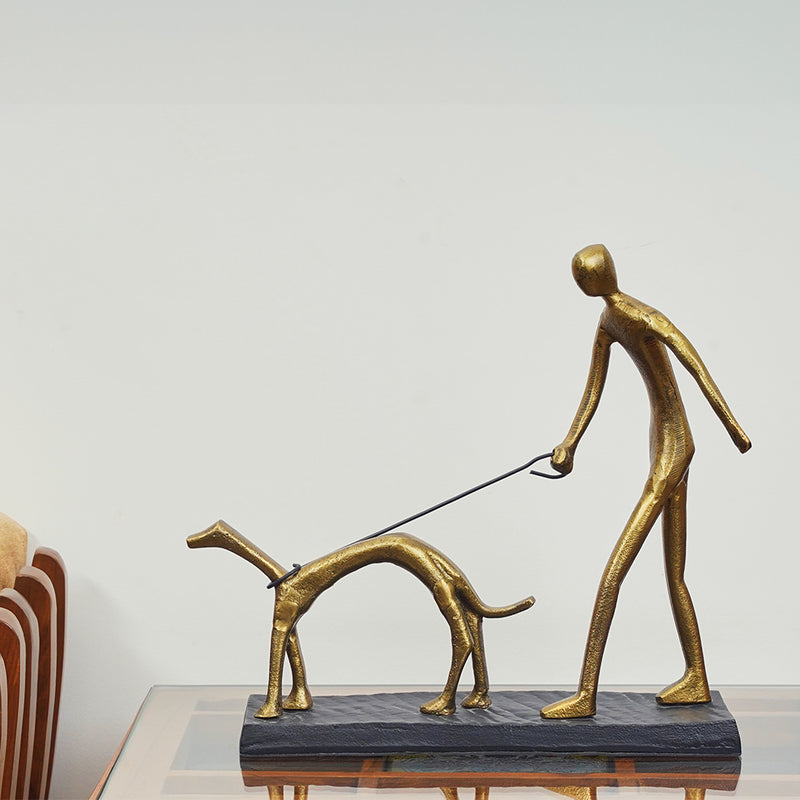 A metallic sculpture of a man walking a dog, placed on a side table.