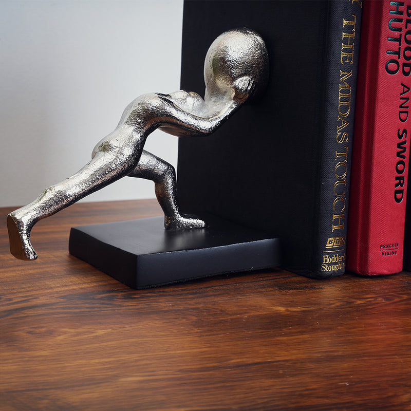 Half of a metallic silver colored bookends set of 2 human figures pushing a book.