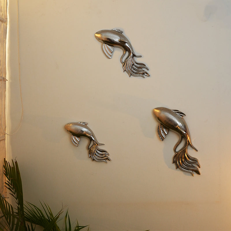 Set of 3 nickel chrome finish metallic wall art fish placed on a wall next to a plant.