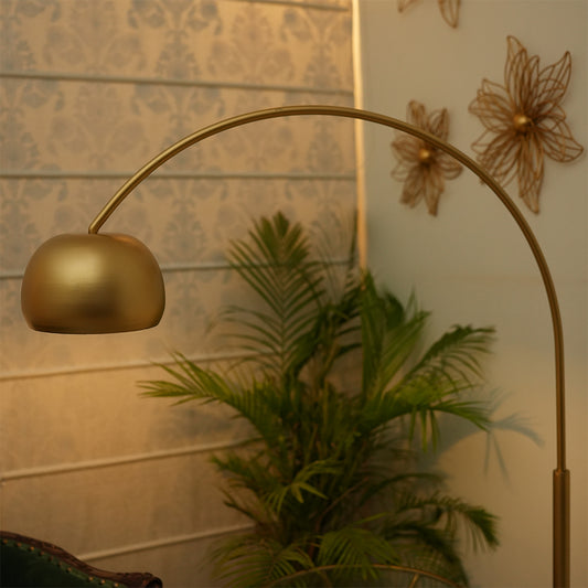 Close-up image of an arched tall metallic floor lamp with a marble base, placed in a living room set-up.