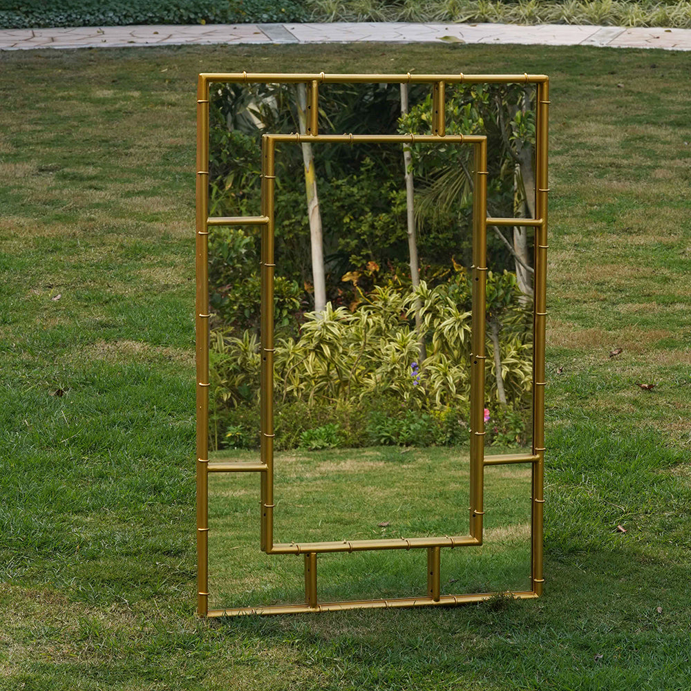 A large rectangular metallic mirror in a bamboo themed frame placed in a garden.