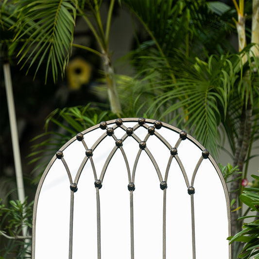 Close-up image of a large bronze finish metallic mirror shaped like a vaulted arched window.