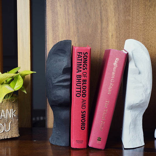 A bookend pair in the shape of an upward looking human face split in half with 2 red cover books in between.