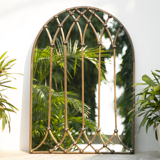 Image of a large bronze metallic mirror shaped like a vaulted window placed against a white wall.