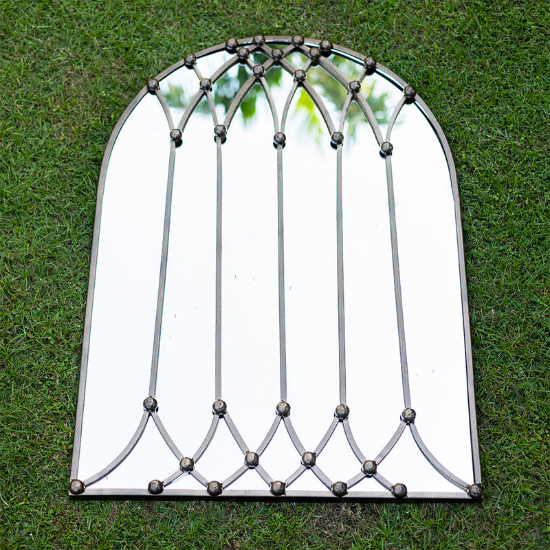 Top view image of a large bronze metallic mirror shaped like a vaulted window placed flat on grass.