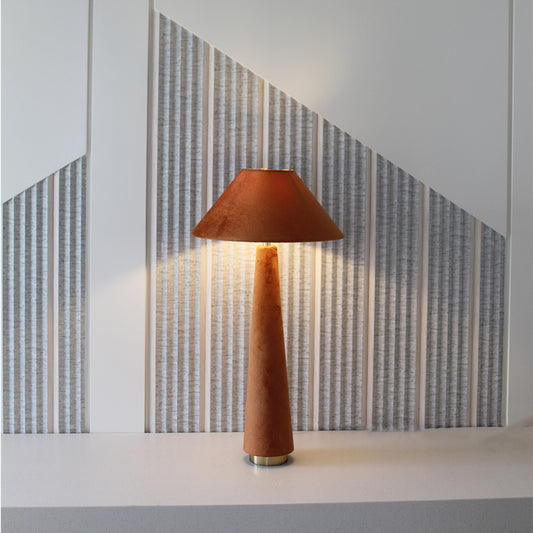 Front view of a orange velvet lamp placed on a console table against a textured wall.