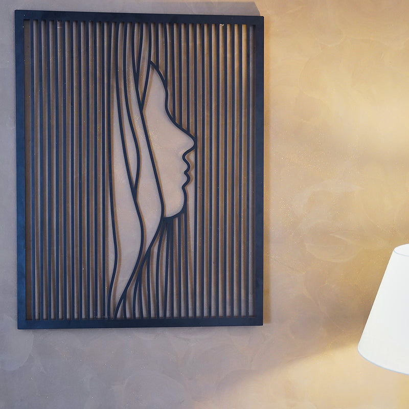 A black metallic wall art in the shape of a woman's face outline displayed on a wall.