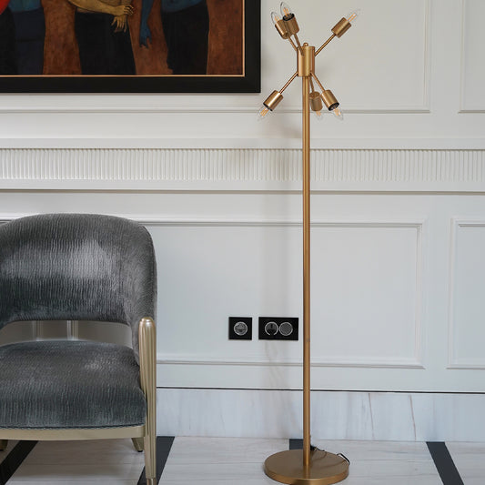 A golden colored modern floor lamp with 6 bulbs is placed in the living room next to a chair.