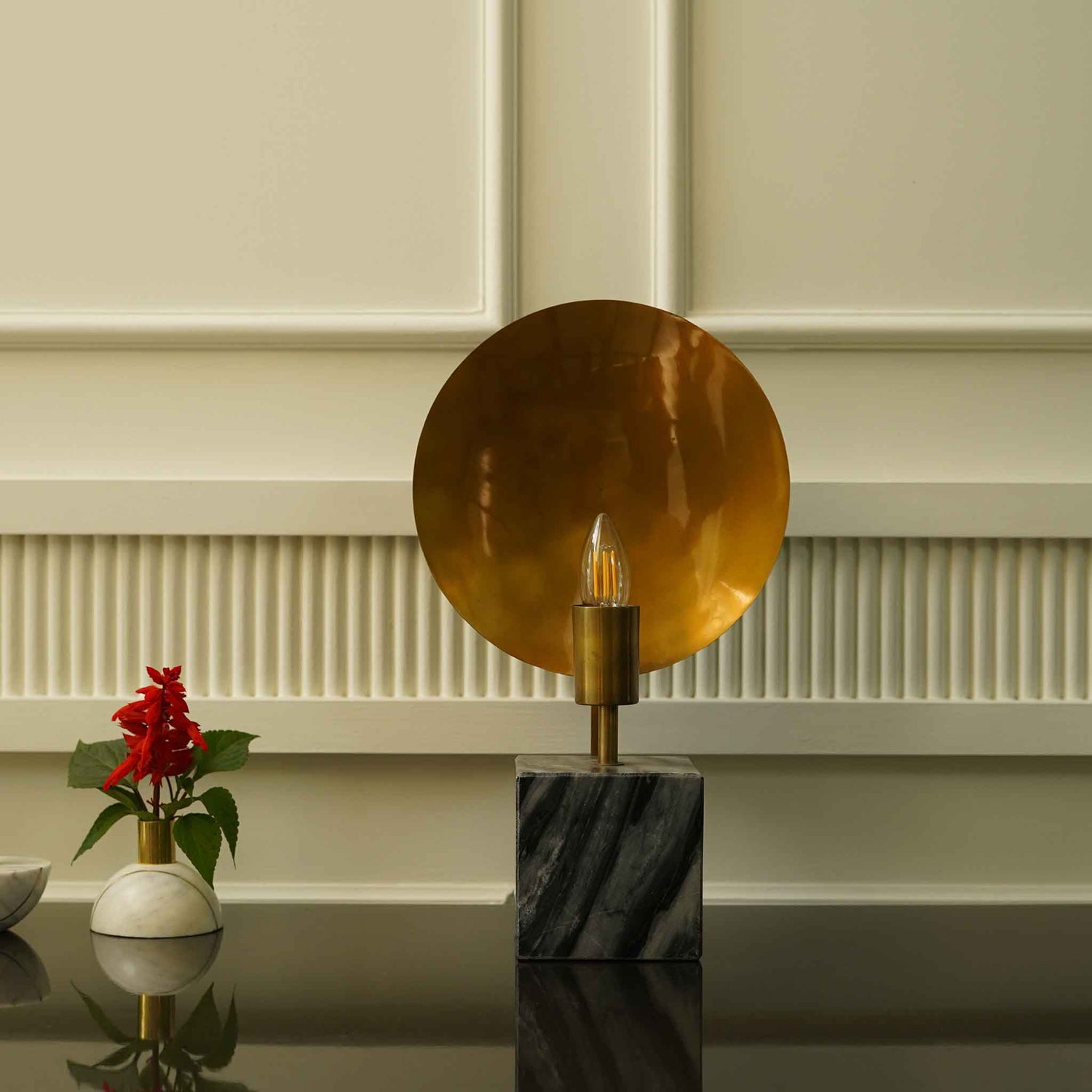Front view of a modern design table lamp on a concrete base and a round metallic plate on the back of the bulb holder.
