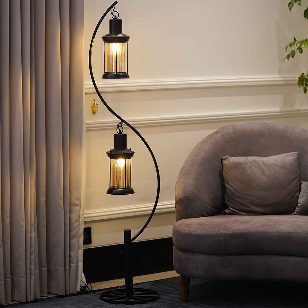 Lit-up modern  metal floor lamp in curved design with two hanging lanterns placed in a living room.