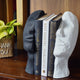 A bookend pair in the shape of an upward looking human face split in half with 3 books in between.