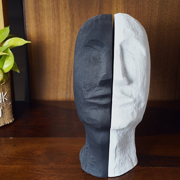 Front view of 2 parts of a bookend set in the design of a human face split in half, one black and other white in color.