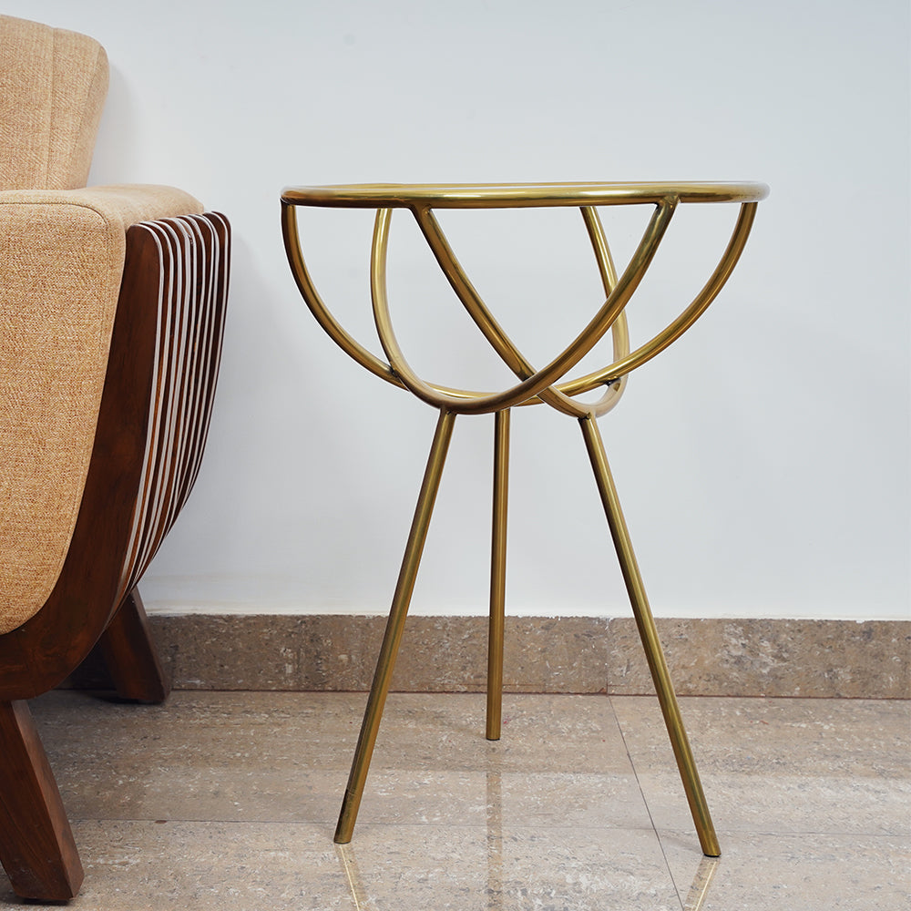 A modern design golden colored metallic side table with a glass top next to a sofa.