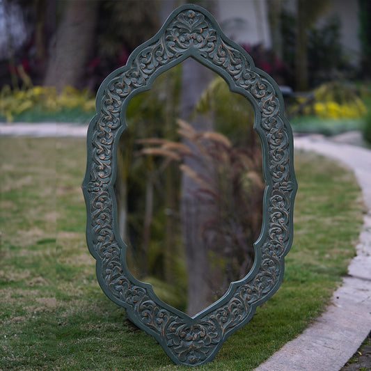 Handcarved green antique finish mango wood frame mirror placed in a garden, front view.
