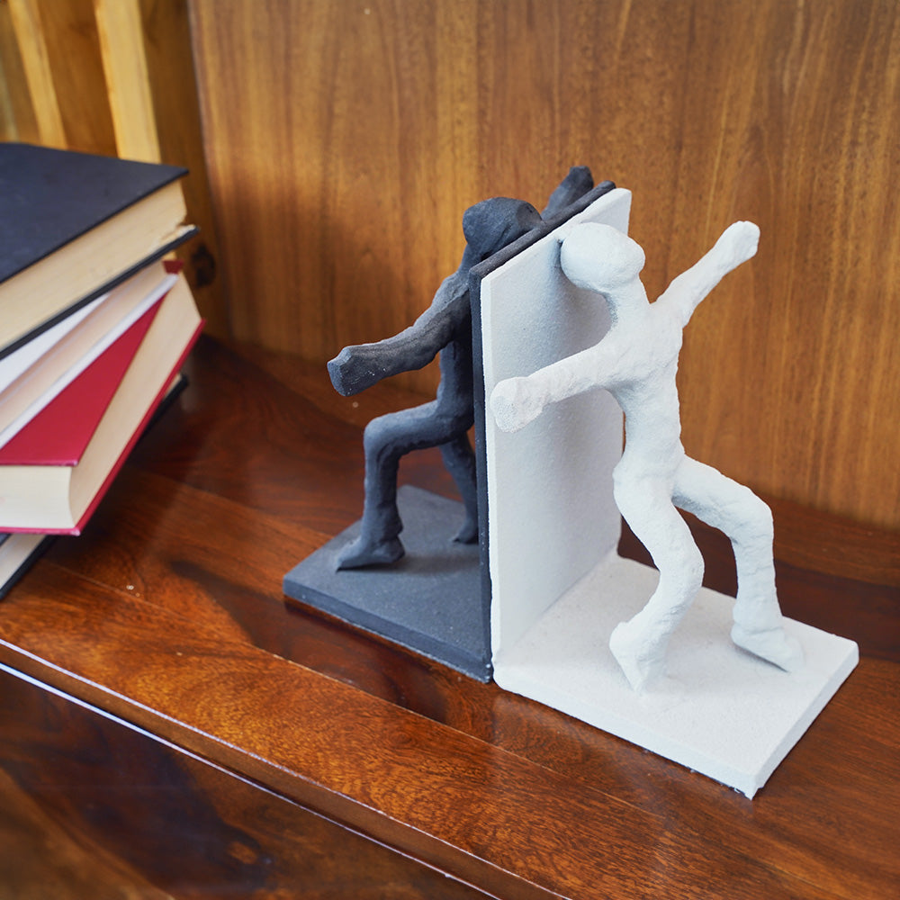 Human figures set of bookends, black one in front and other white on the back side, with books stacked next to them.