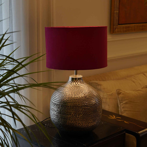 Handmade metal table lamp with holes on surface and paired with a red lamp shade.