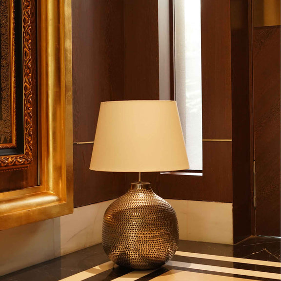 Large handmade metallic lamp with holes on the metal surface, placed on the floor.