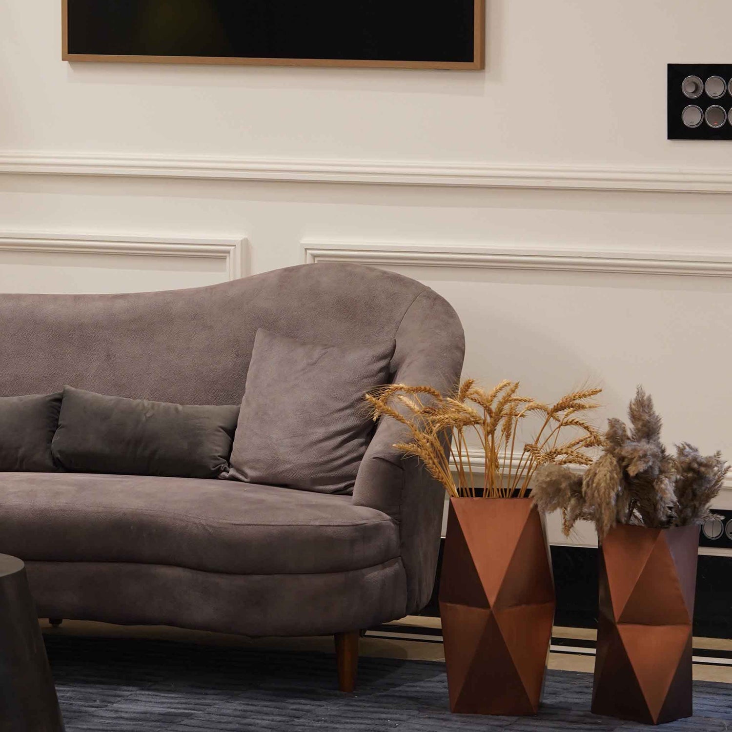 Two large hexagonal metallic vases in copper finish placed on the floor next to a sofa.