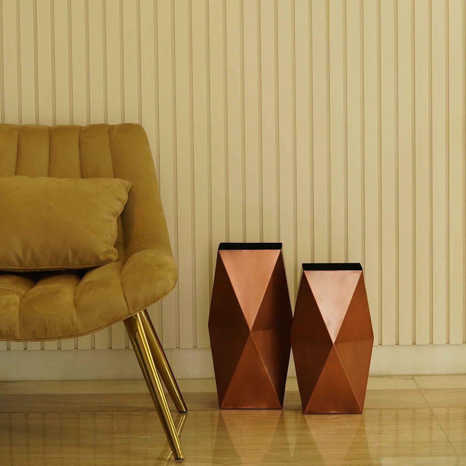 Two large hexagonal metallic vases in copper finish placed on the floor next to a chair.
