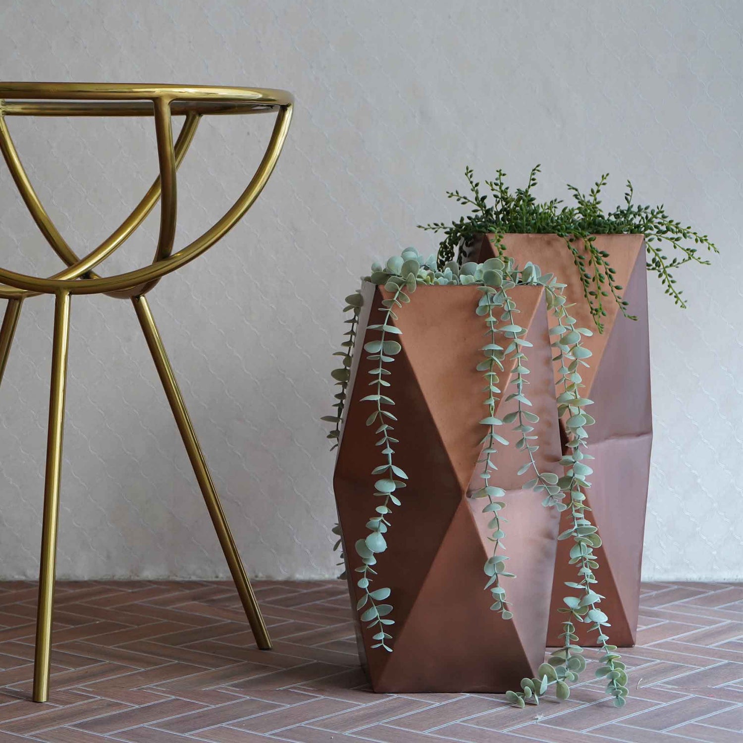 Two large hexagonal metallic vases in copper finish placed on the floor next to a table.