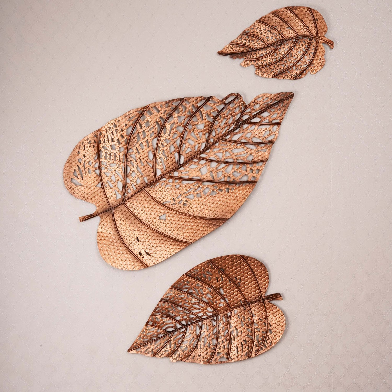 Set of 3 metallic leaves wall art in a plain background.