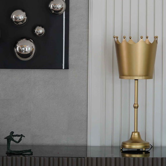 Imperial design golden metallic table lamp with a crown shaped shade placed on a console table.