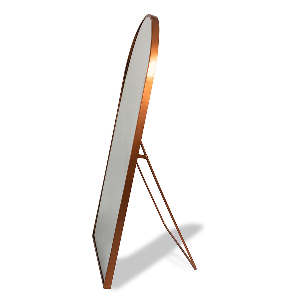 A curved metallic full length floor mirror  with a back stand in a plain white background.