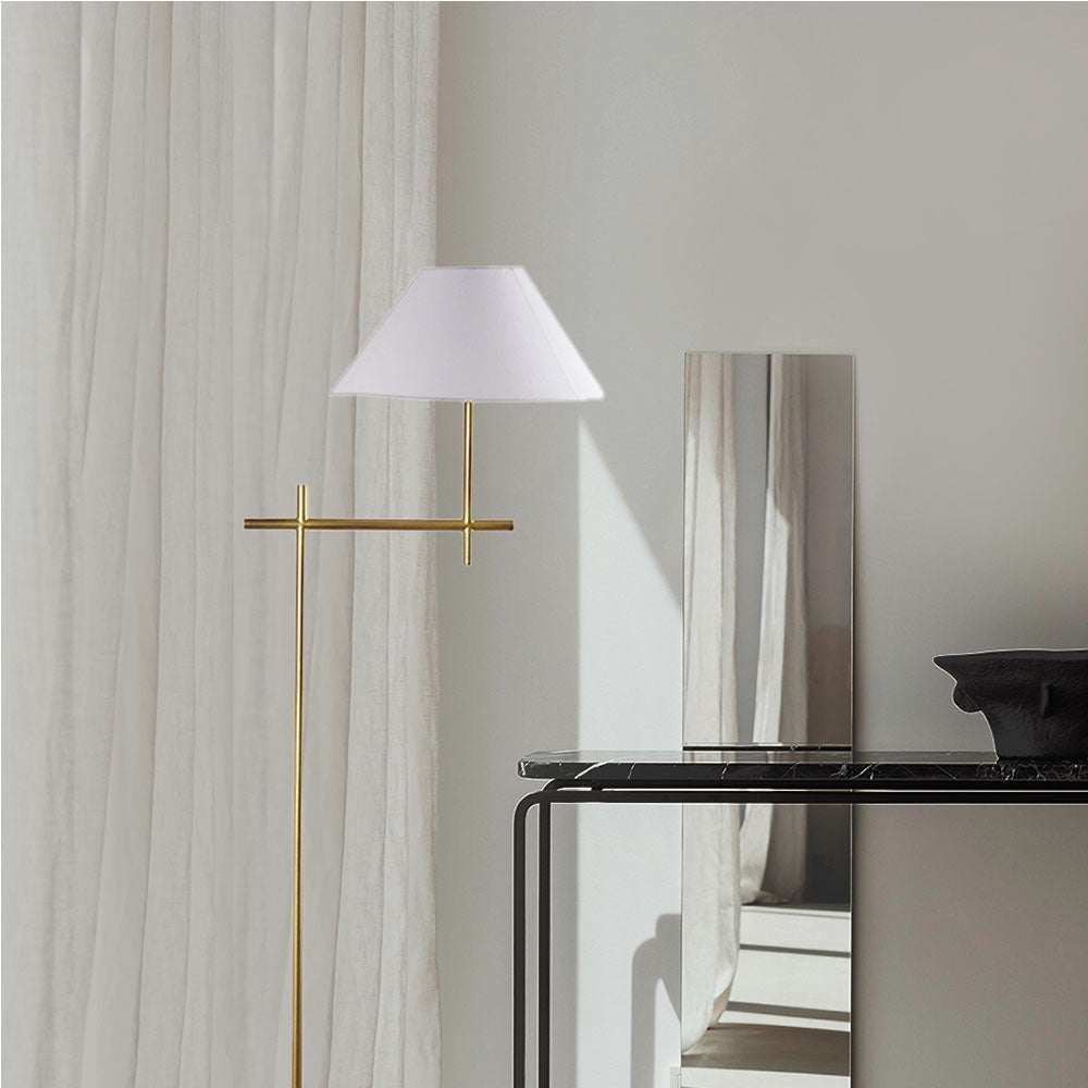 Tall, minimalistic design golden floor lamp with shade next to a black console table in front of a mirror.