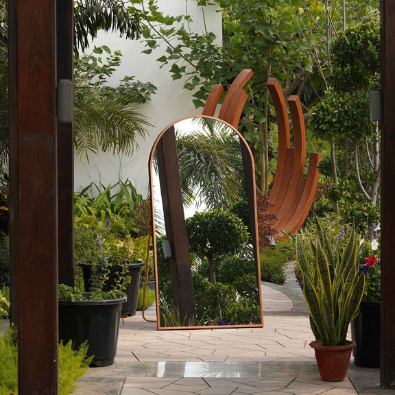 Front view of a curved metallic full length floor mirror in outdoor setting.