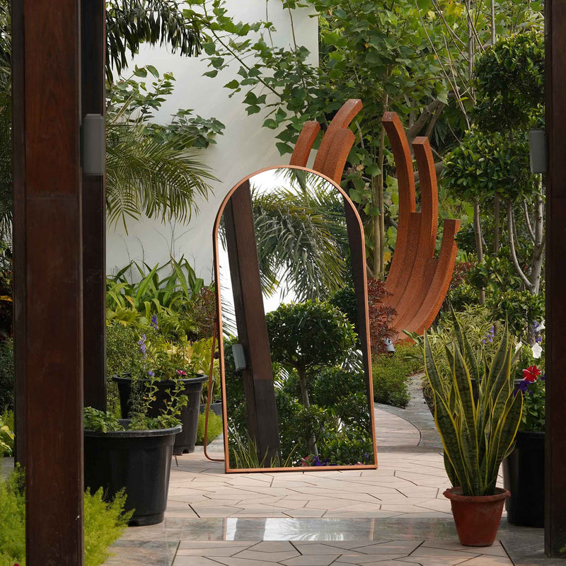 Front view of a curved metallic full length floor mirror in outdoor setting.