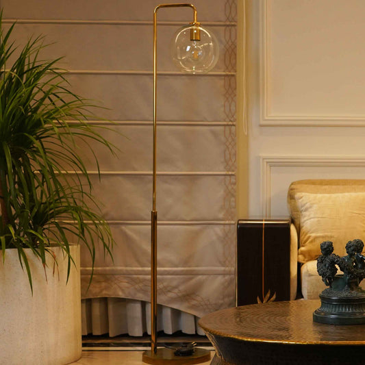 A golden slim metallic floor lamp ending in a round globe glass is placed in a living room.