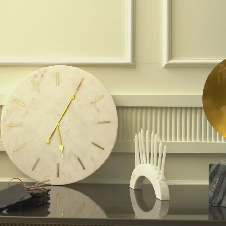 Close-up short video of a large and heavy white marble clock with golden hands and hours marked with brass inlay.