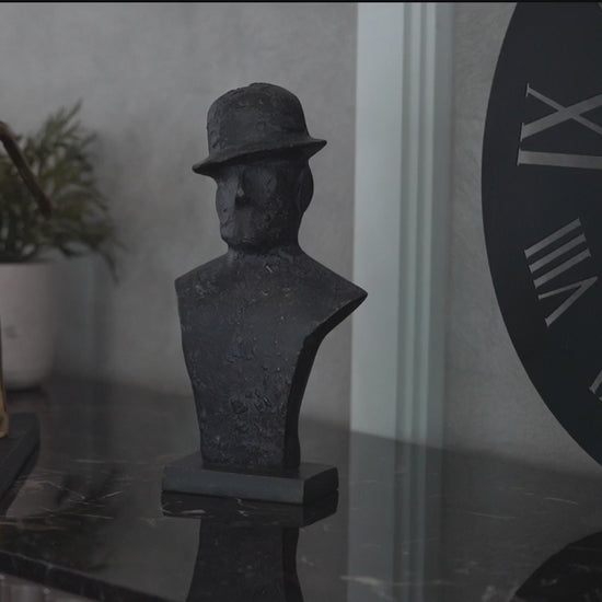 Close-up short video of a black metallic table-top sculpture of a man wearing a tilted hat.