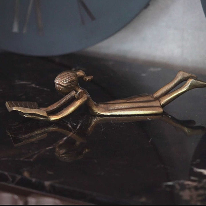 Zoomed video of a table-top metallic decorative girl figurine lying down and reading a book.