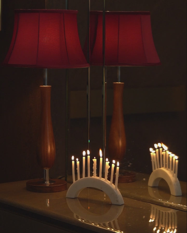 Short video of a wooden table lamp with a red lampshade placed next to burning candles on a candle holder in front of a mirror.