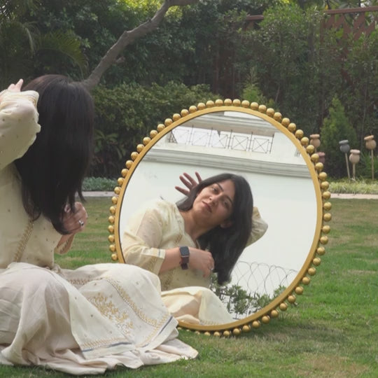 Video of a model making her hair in front of a large round metallic mirror.