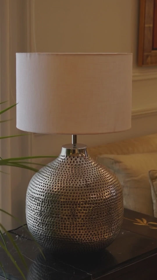 Video of a round metallic perforated table lamp with different lamp shades and the lights being turned on and off.