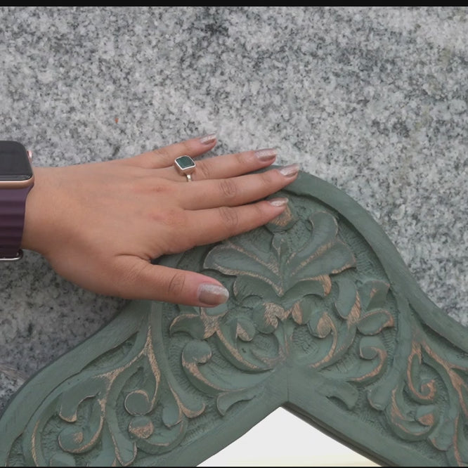 Video showing close up of a woman feeling the carving on the wooden frame of a mirror