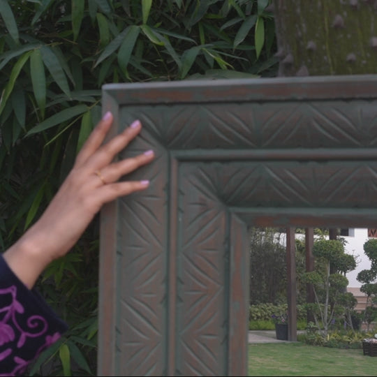 Close up video of a female hand feeling the ridges and carvings of a long wooden mirror.