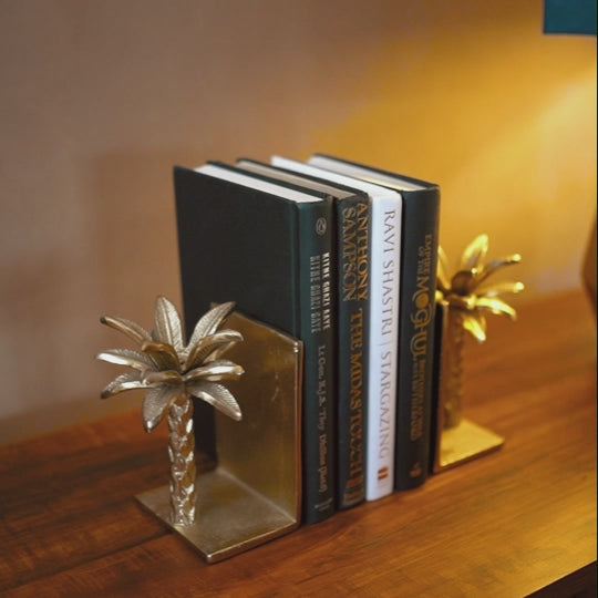 Video of a lady pulling out a book from a set of golden metallic palm tree shaped bookends with 4 books placed in between.