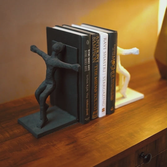 Video of a woman pulling out a book from a stack of books placed between two human figures bookends set.