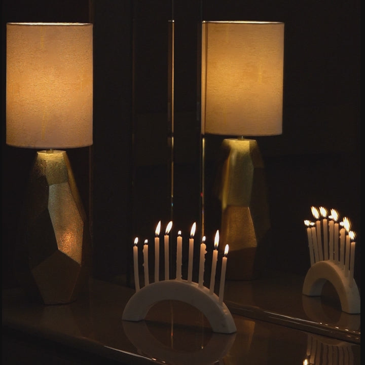 Golden color metallic textured table lamp placed next to a mirror and burning candles on a marble candle holder.