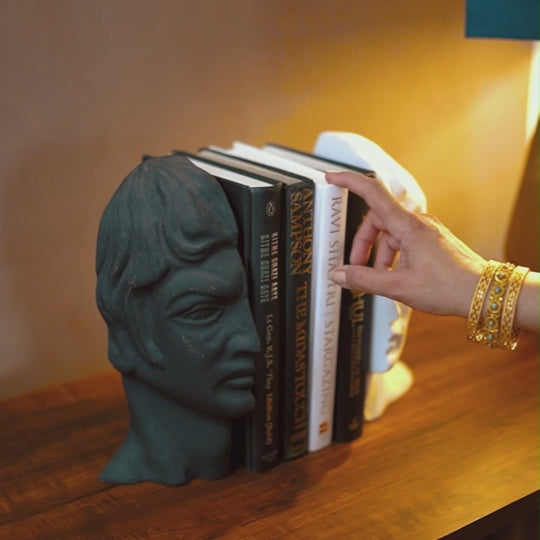 A woman pulling out a book from a stack of books placed between a set of human face bookends.