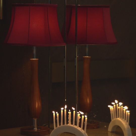 Short video of a wooden table lamp with a red lampshade placed next to burning candles on a candle holder in front of a mirror.