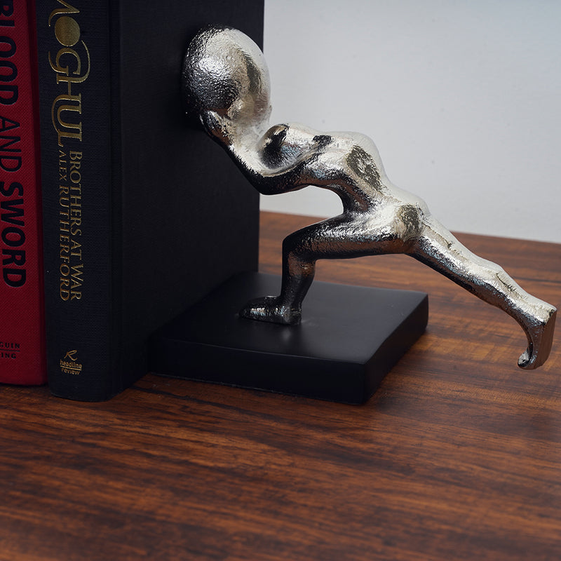 Half of a metallic silver colored bookends set of 2 human shapes pushing a book.