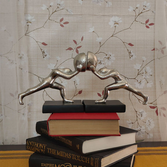 Metallic silver colored bookends set of 2 human figures pushing from opposite direction on top of 4 books stacked on one another.