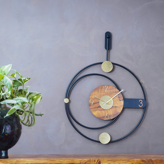 Modern design large metallic wall clock in rings shape design, placed on a wall in front of a console table on which a plant is placed.