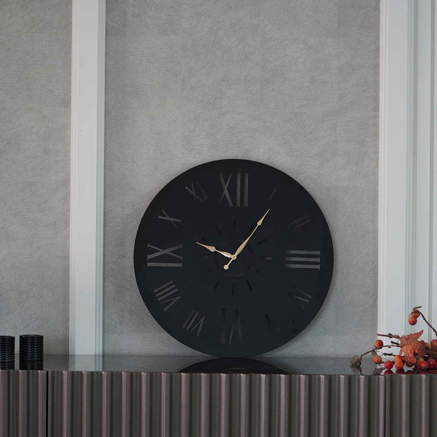 A large black wall clock with golden hands placed on a console table.