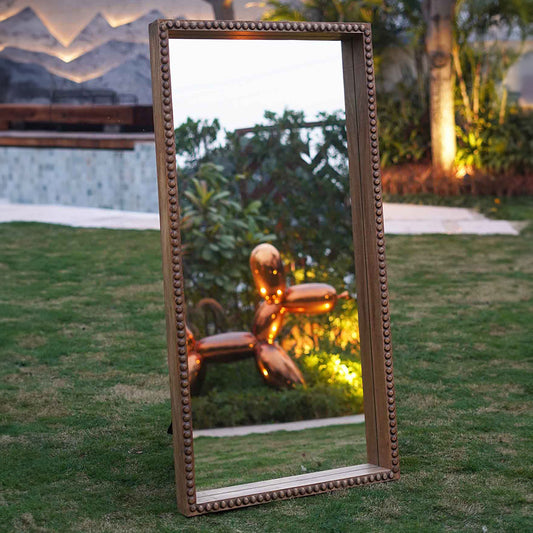Large floor mirror in hand carved mango wood frame placed in a garden.