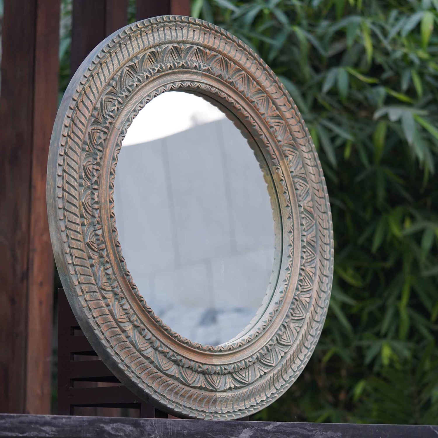 Large circular mirror in hand-carved mango wood frame- side view.